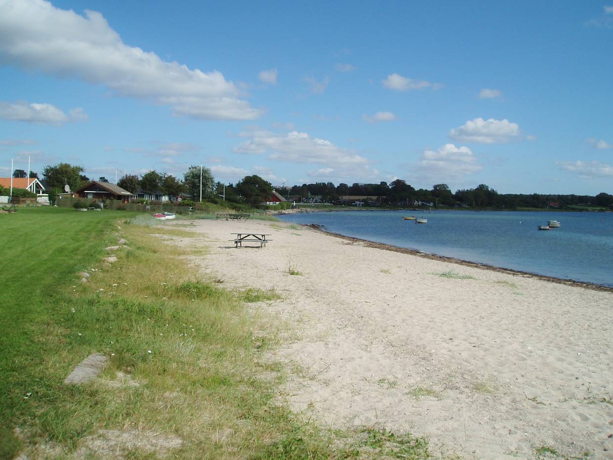Schmaler Sandstrand, im Hintergrund Ferienhäuser mit Meerblick