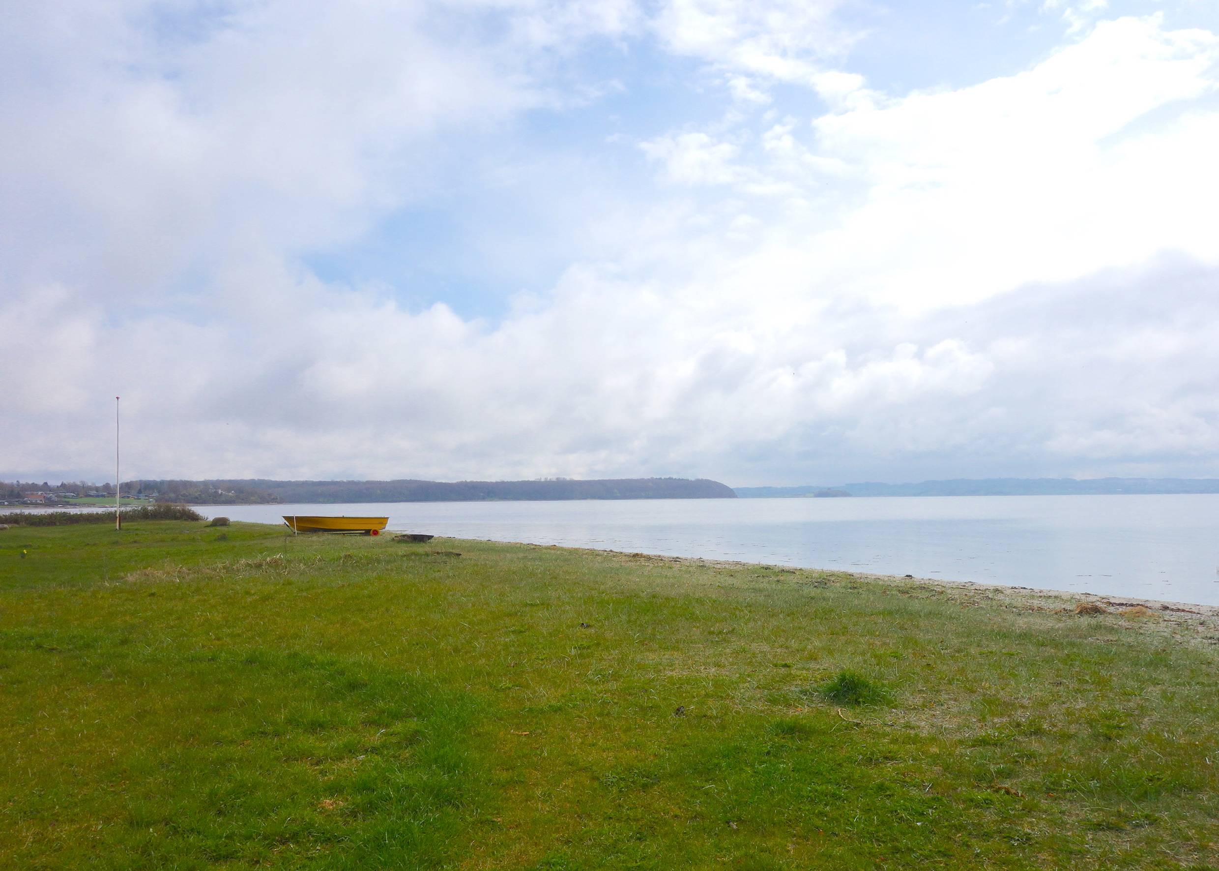 Rasenfläche am Ufer, im Hintergrund ein orangenes Ruderboot