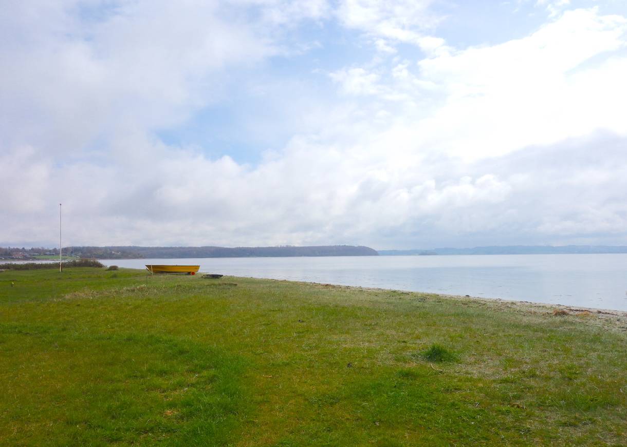 Rasenfläche am Ufer, im Hintergrund ein orangenes Ruderboot