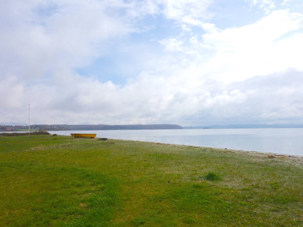 Rasenfläche am Ufer, im Hintergrund ein orangenes Ruderboot