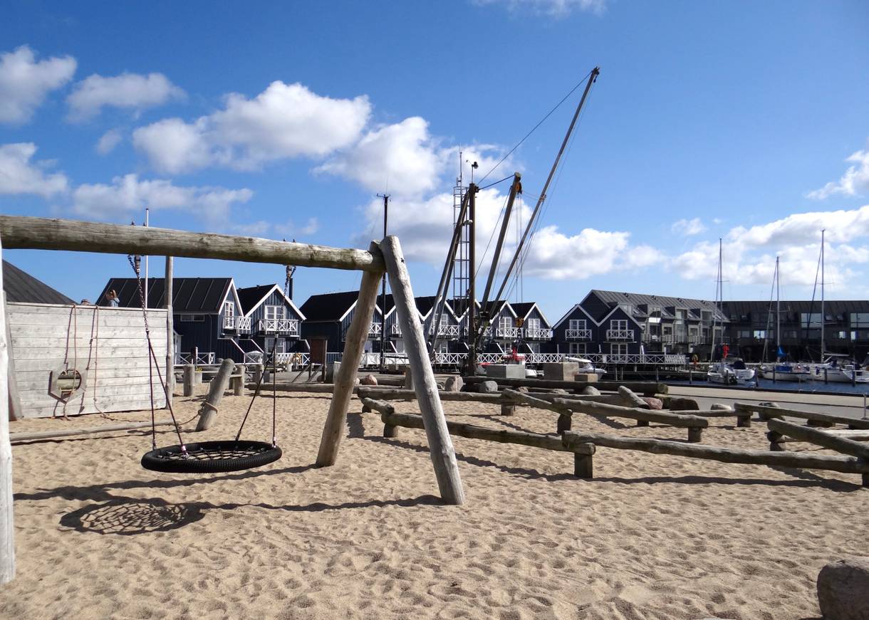 Schaukel in einem großen Sandkasten, im Hintergrund Reihenhäuser