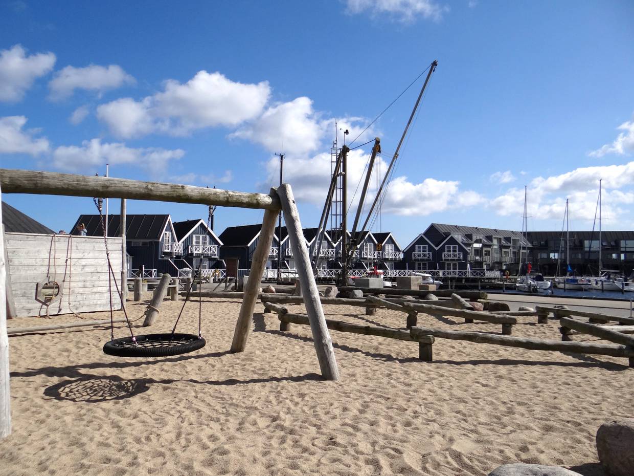 Schaukel in einem großen Sandkasten, im Hintergrund Reihenhäuser