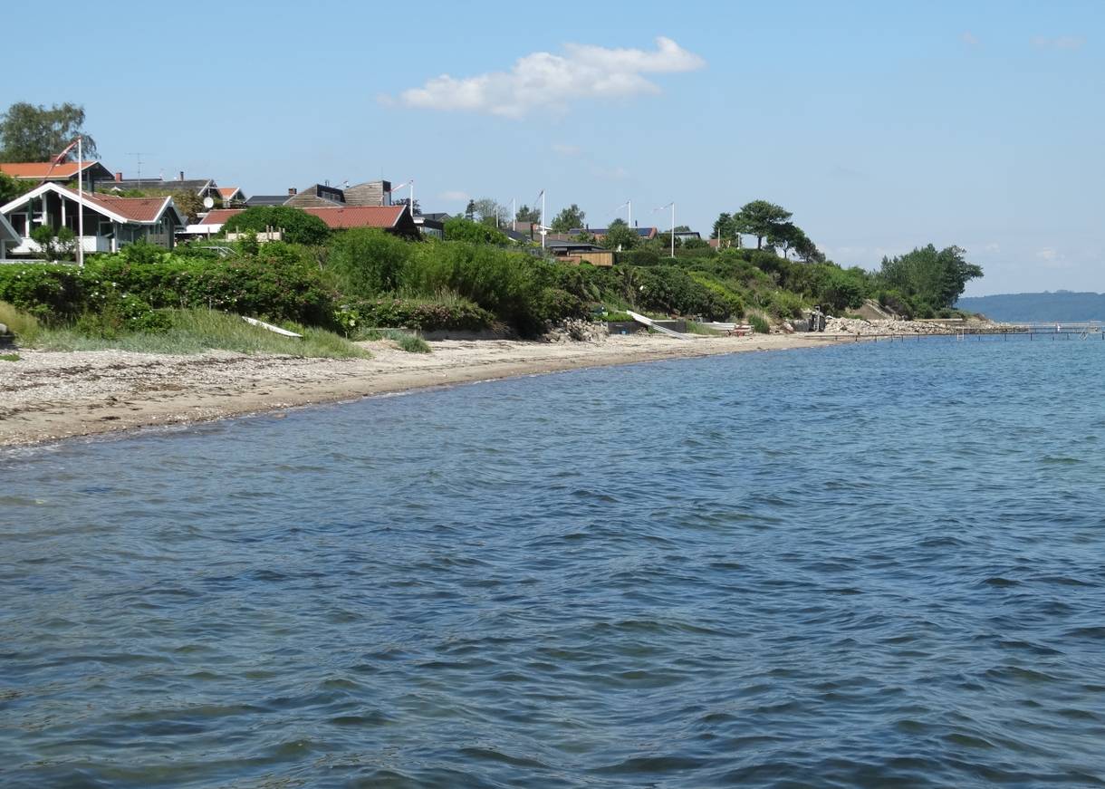 Steiniger Strand am Fjord, am Ufer Ferienhäuser