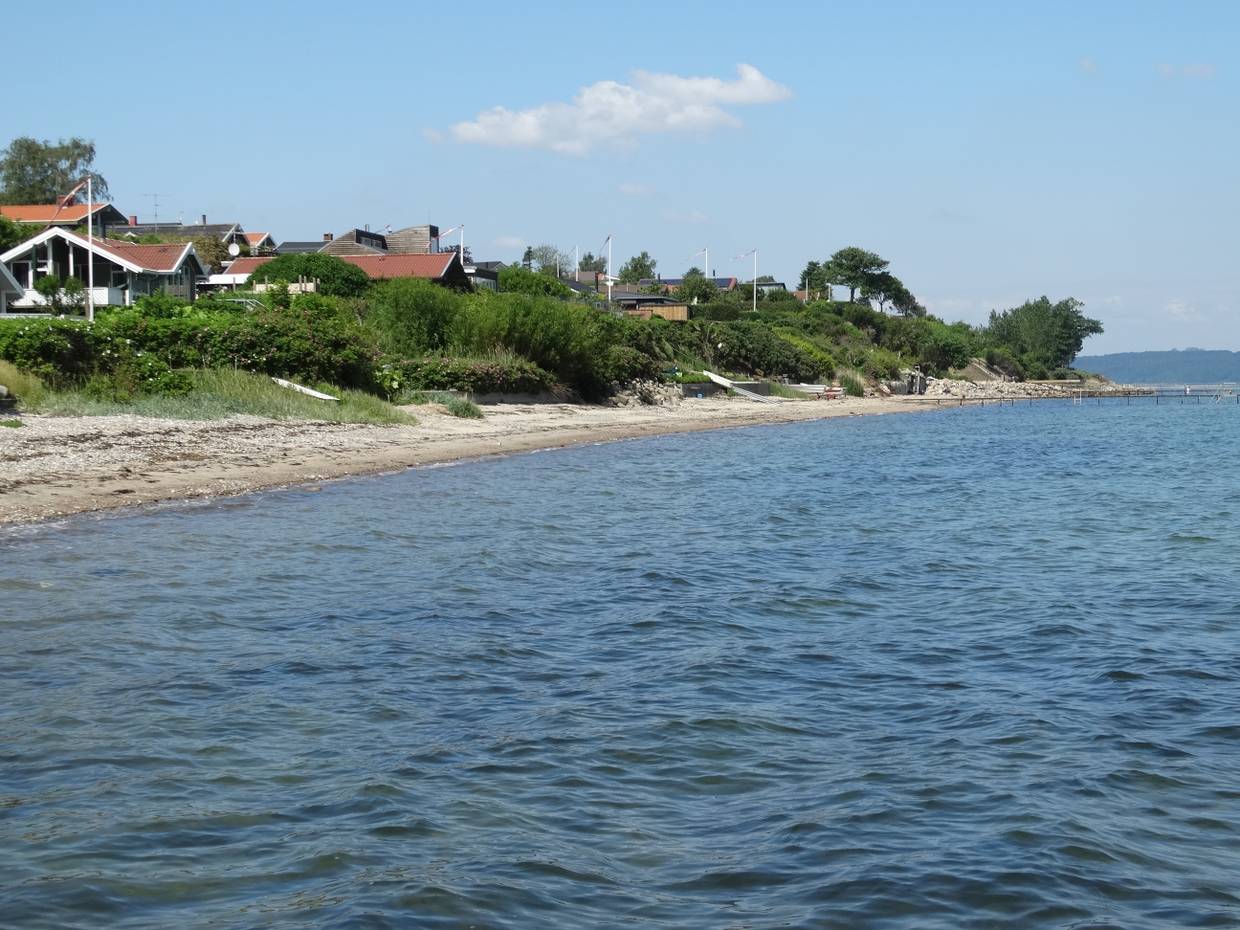 Steiniger Strand am Fjord, am Ufer Ferienhäuser