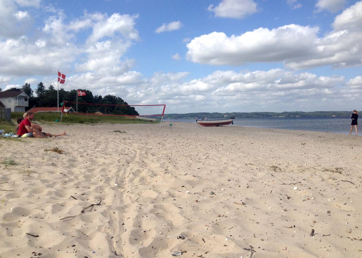 Weg durch Strandwiesen, dazwischen etwas Sand, im Hintergrund Ferienhäusern