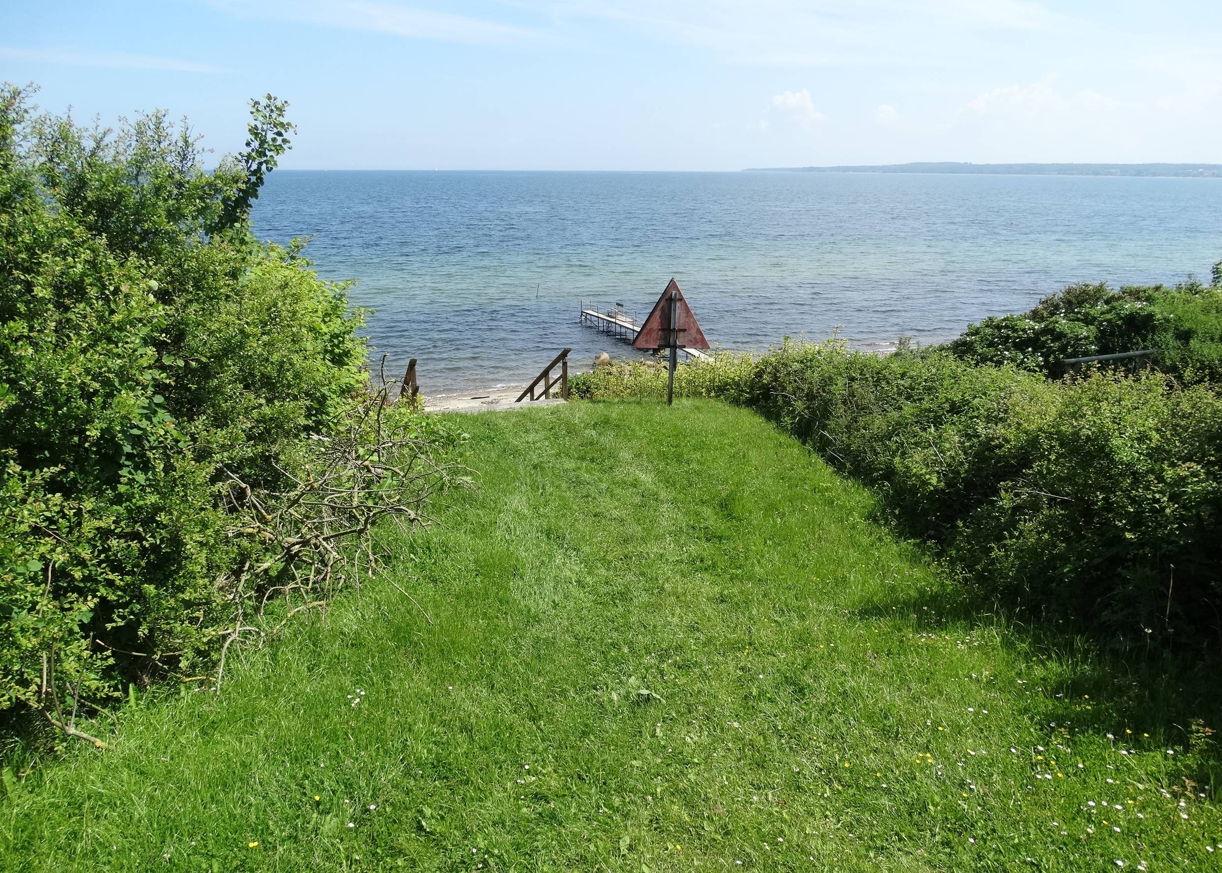 Grüner Pfad zwischen Büschen zu einer Treppe, die zum Wasser führt