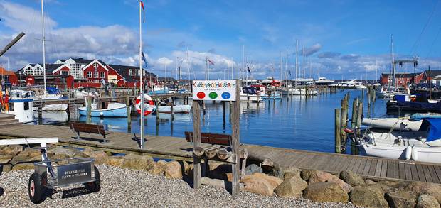 Aussicht über ein Hafenbecken mit Fischer-, Ruder, und Segelbooten, große, rote Gebäude umranden das Becken
