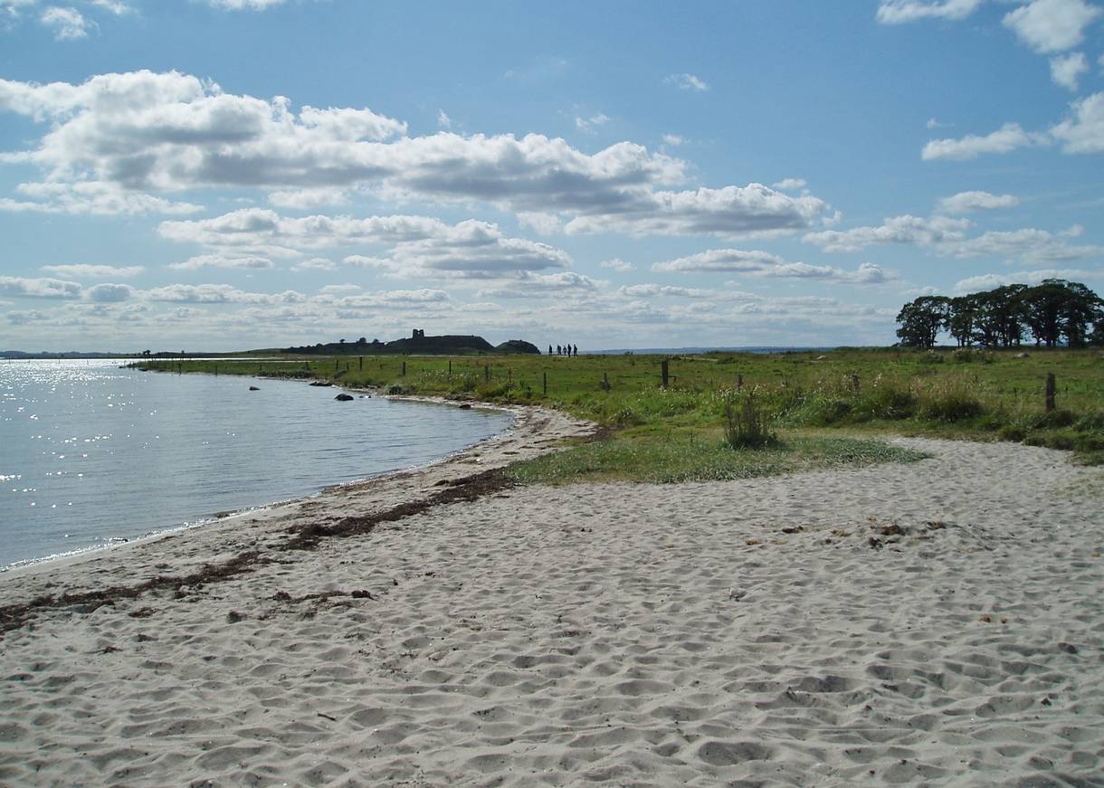 Sandstrand, im Hintergrund Wiesen und die Silhouette der Schlossruine
