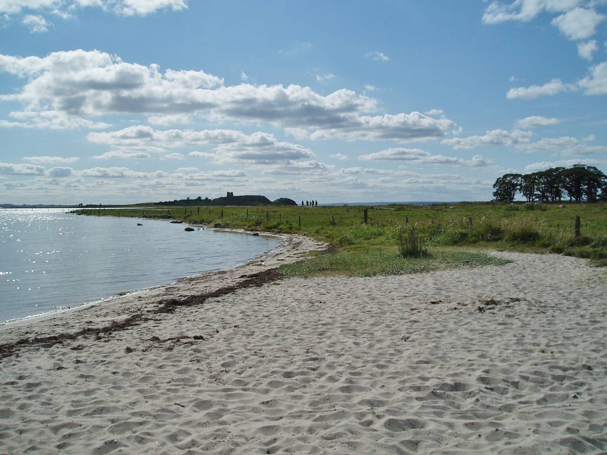 Sandstrand, im Hintergrund Wiesen und die Silhouette der Schlossruine