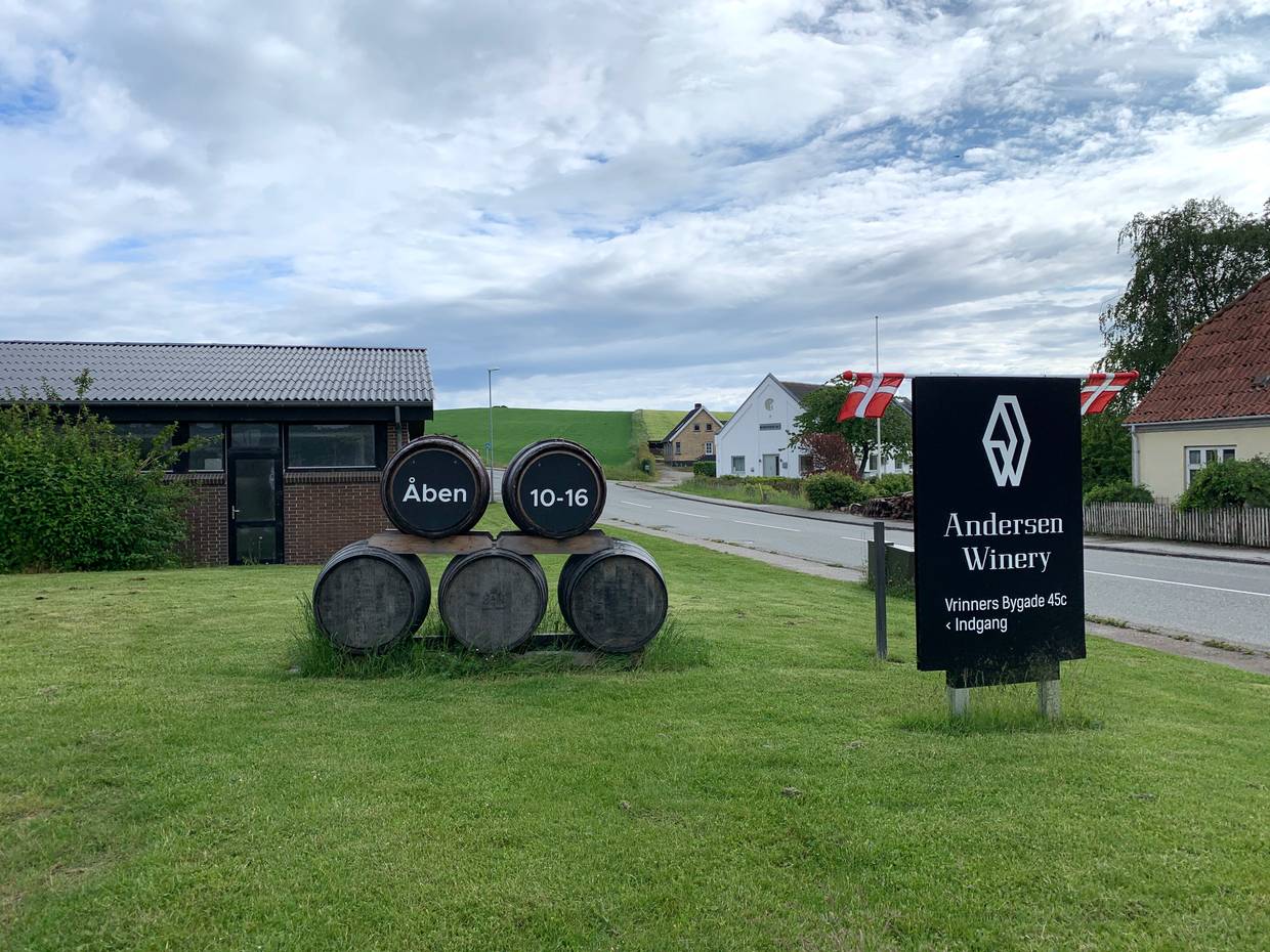 Gestapelte Weinfässer auf der Wiese vor einem Haus mit Öffnungszeiten zum Hofladen der Winery