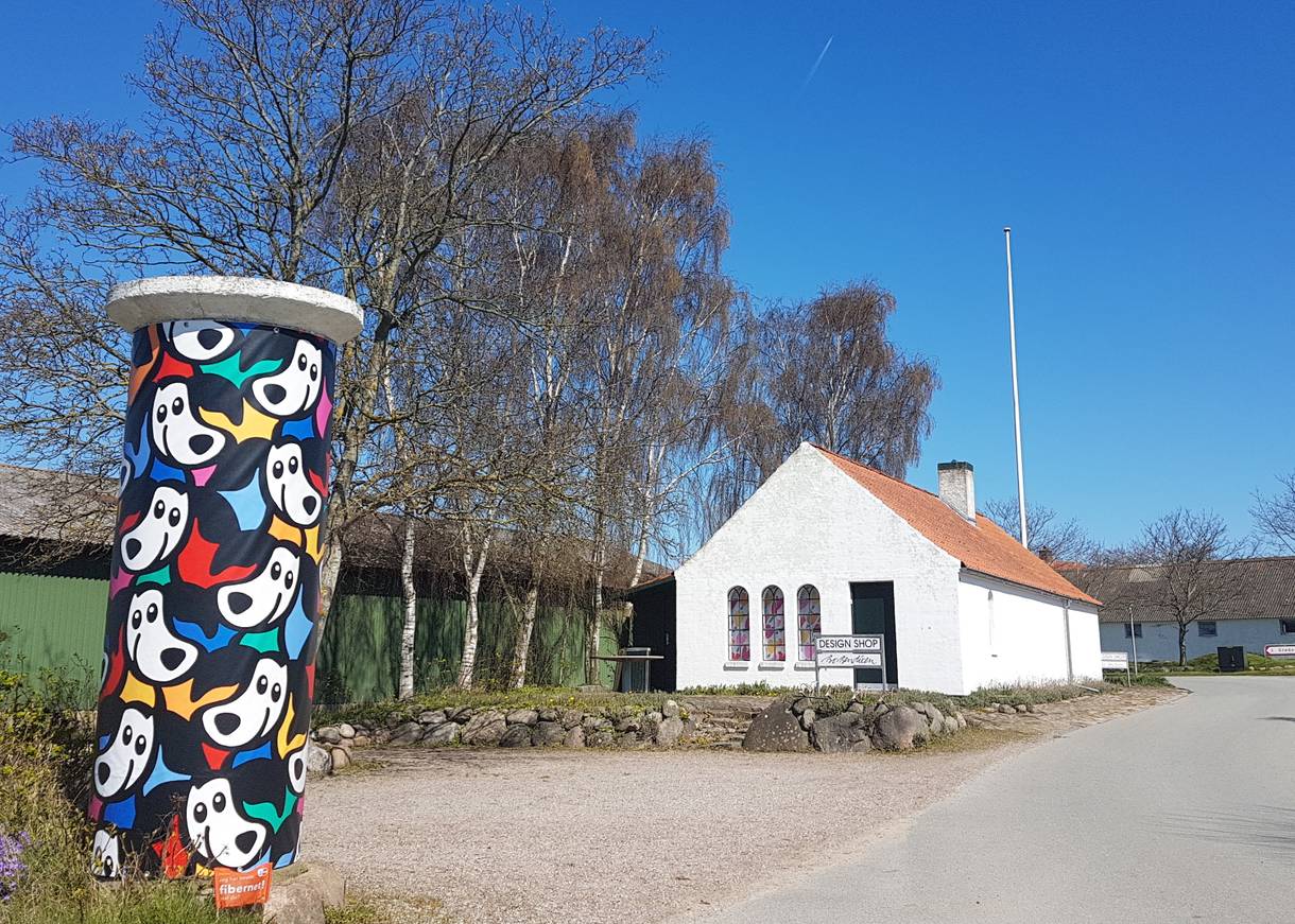 Litfaßsäule mit bunten Figuren an einer Dorfstraße