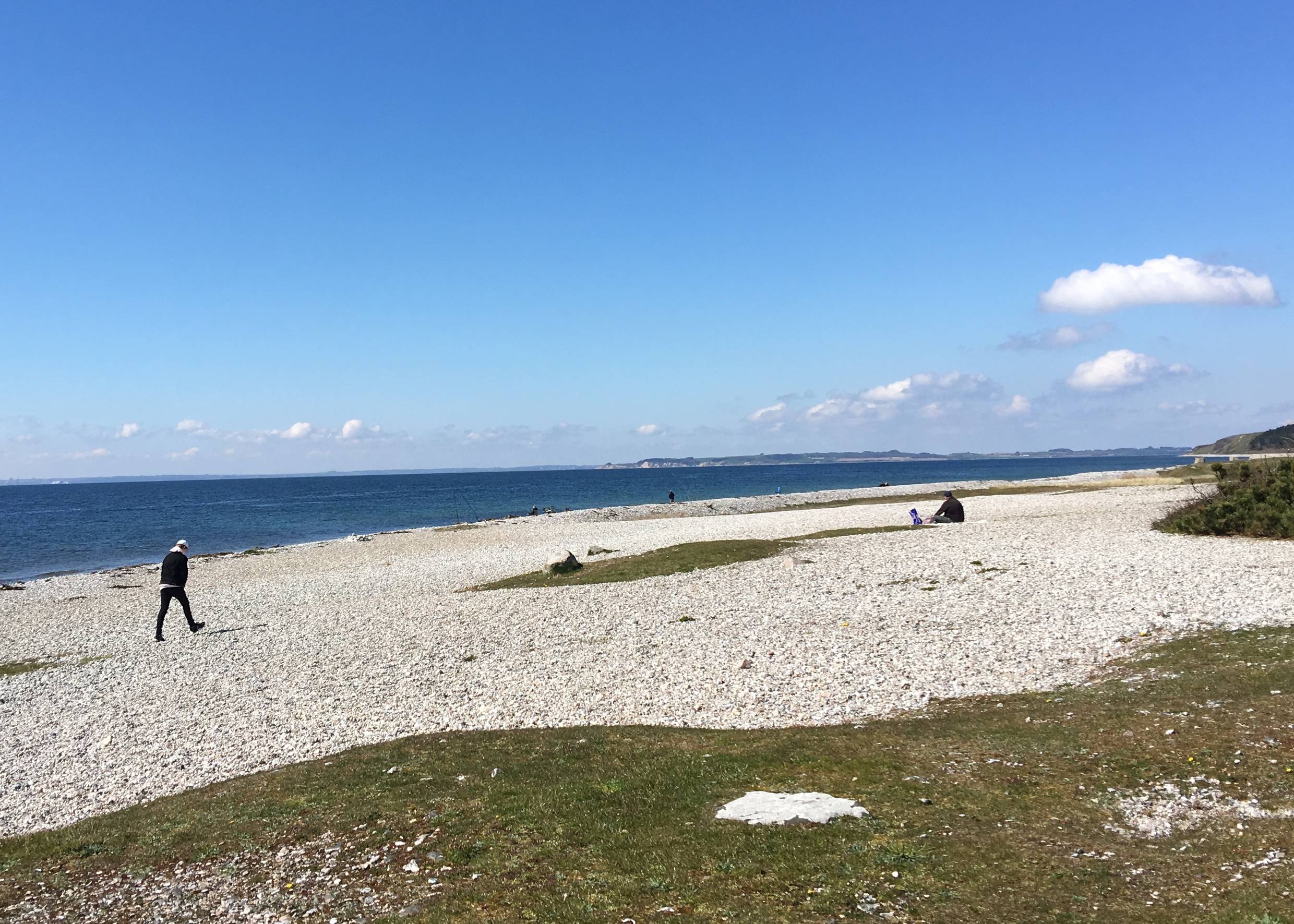 Weißer Strand aus dicken Kieselsteinen mit Spaziergängern