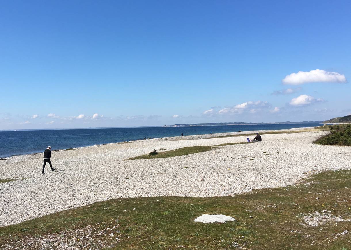 Weißer Strand aus dicken Kieselsteinen mit Spaziergängern