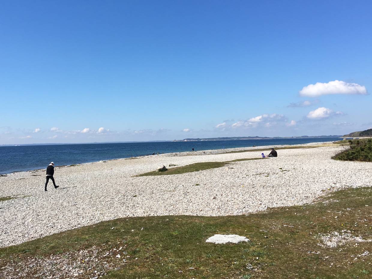 Weißer Strand aus dicken Kieselsteinen mit Spaziergängern