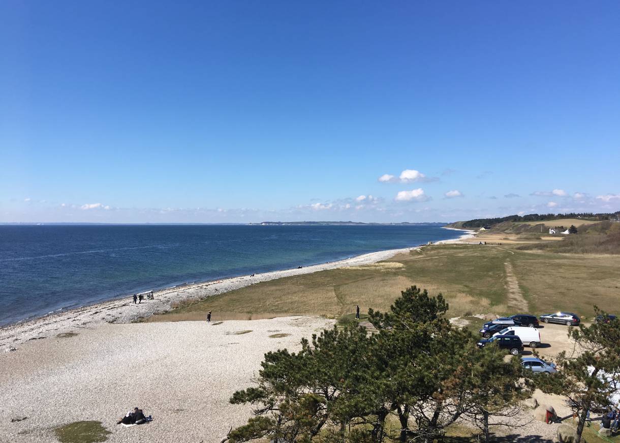 Blick vom Leuchtturm auf Helgenæs auf einen steinigen Strand, im Hintergrund Steilküste