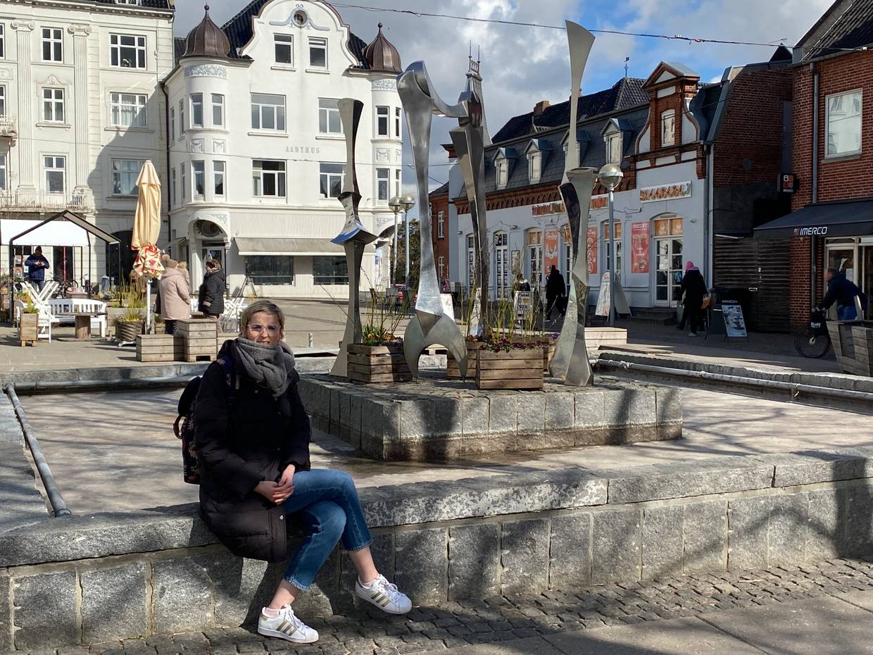 Brunnen mit Kunstinstallation vor einem weißen Bürgerhaus, eine Frau sitzt am Brunnen