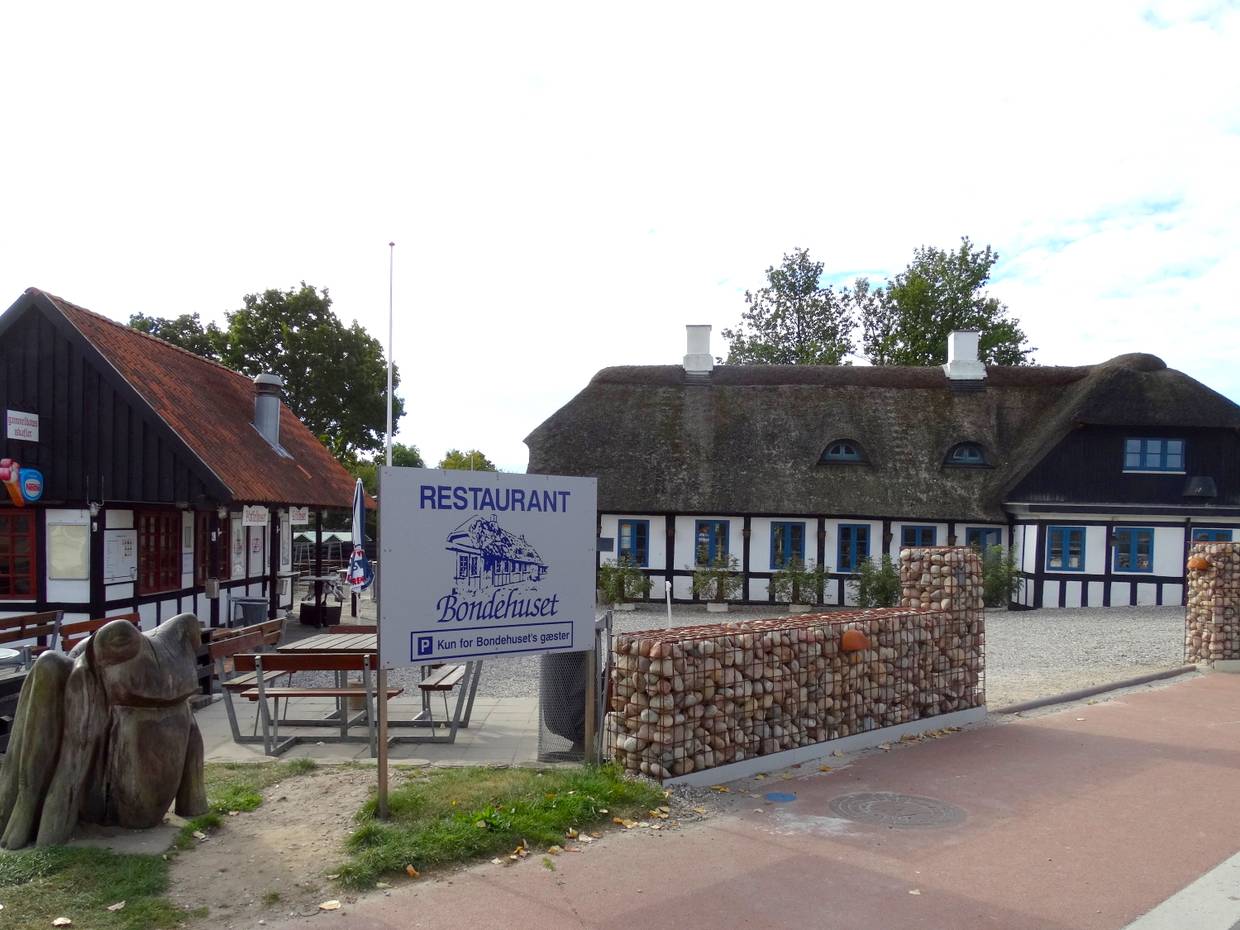 Fachwerkhaus mit Parkplatz davor, links ein Kiosk und eine Skuptur 