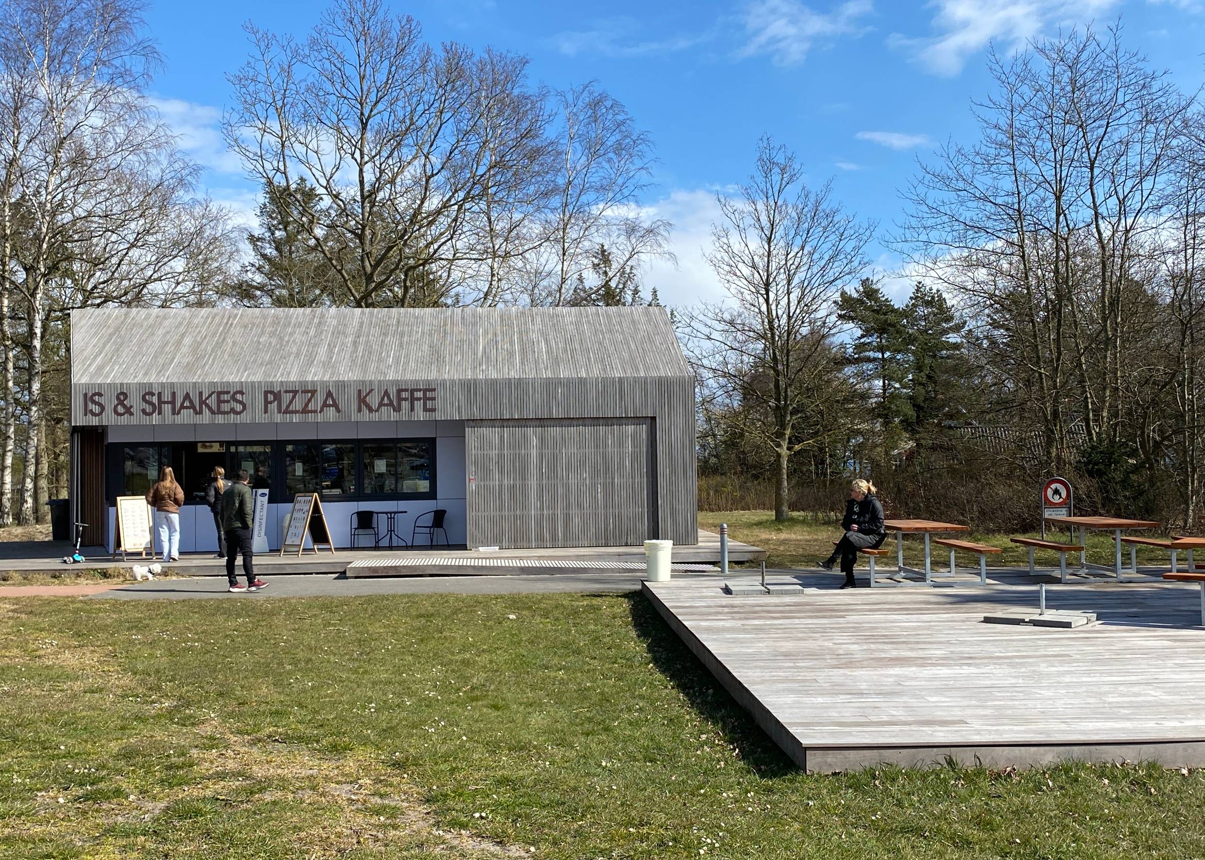 Holzkubus als Strandkiosk, davor eine hölzerne Terrasse
