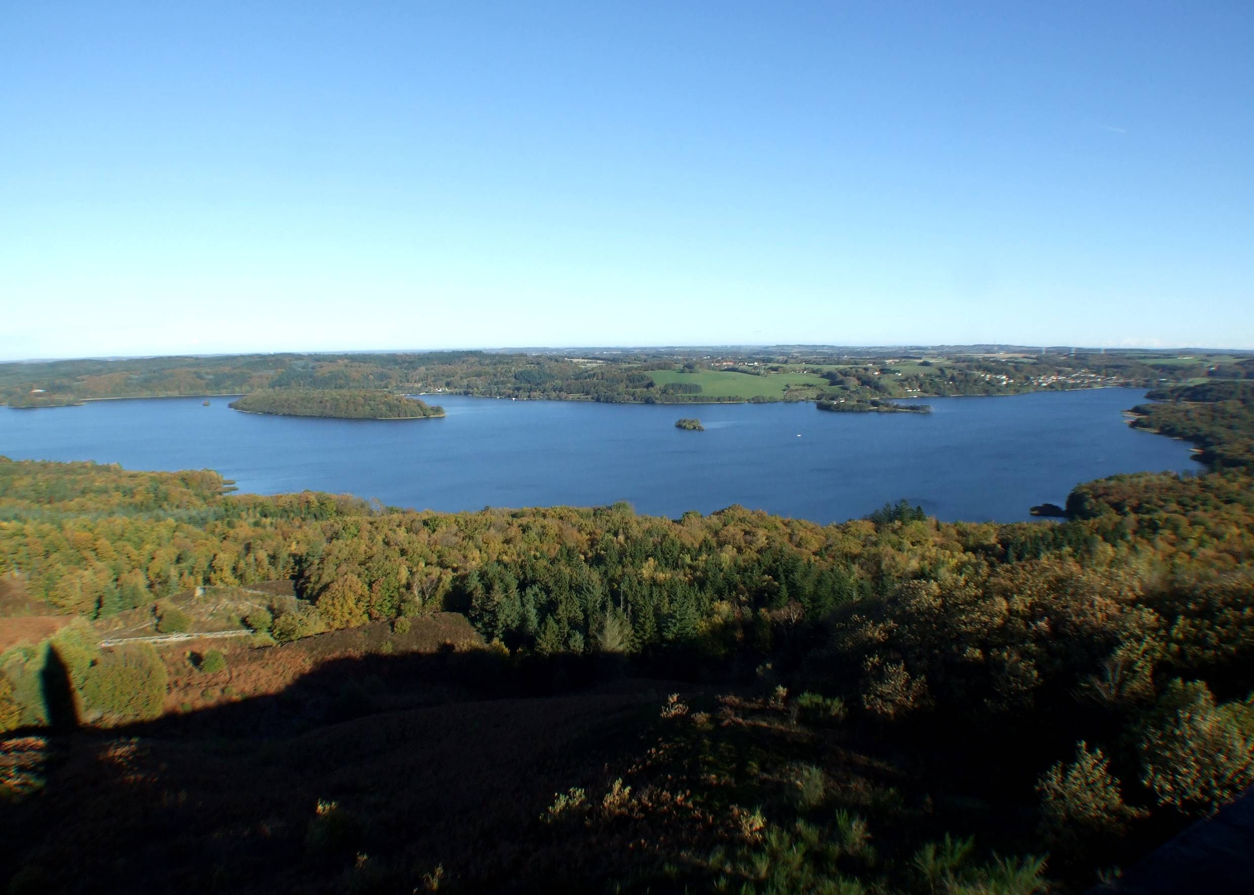 Blick auf eine See im Herbstwald von oben, der Schatten eines Turmslinks im Bild