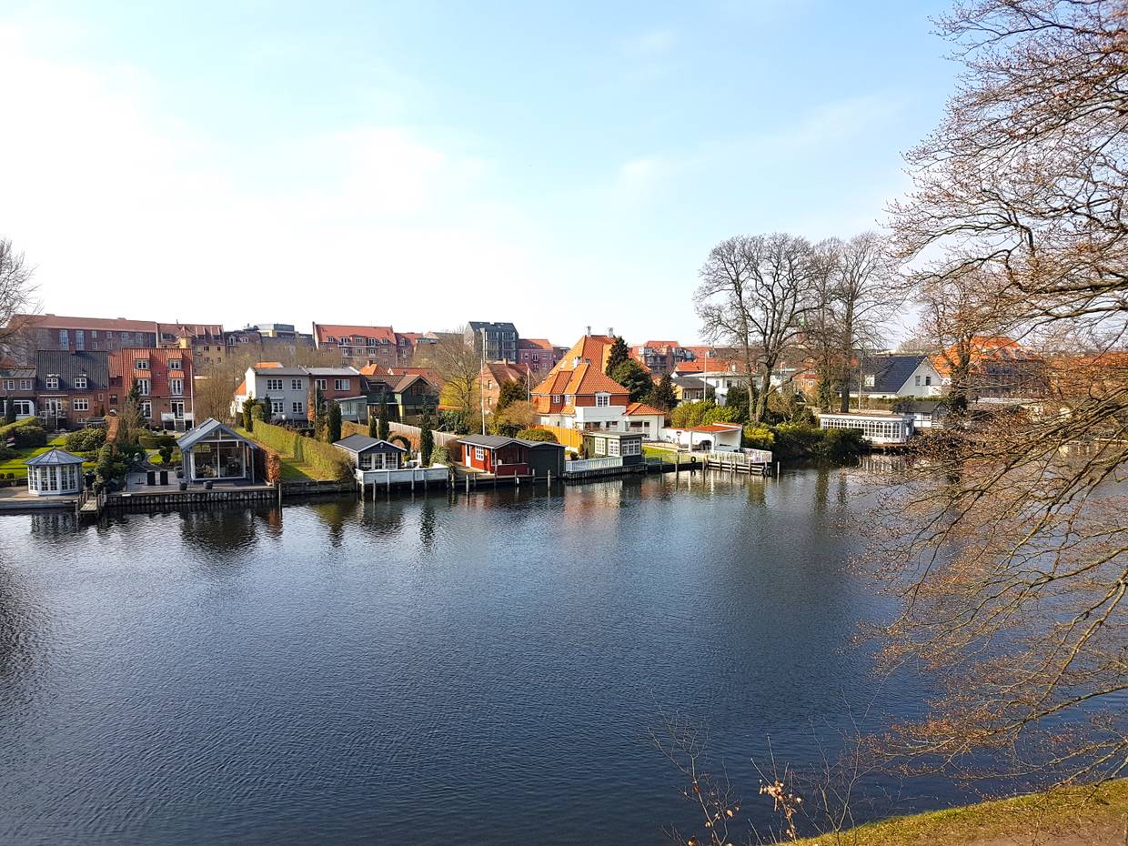 Blick über einen Fluss, am gegenüberliegenden Ufer stehen Häuser direkt am Wasser