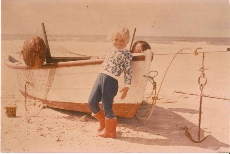 Mädchen lehnt an einem kleinen Fischerboot am Strand