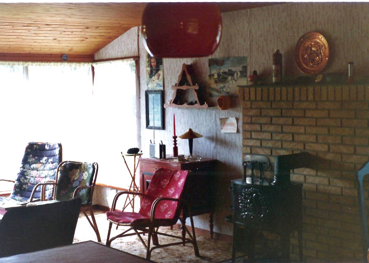 Wohnraum in den 70ern mit einem Kamin, Korbsesseln und Kitschbilder an den Wänden