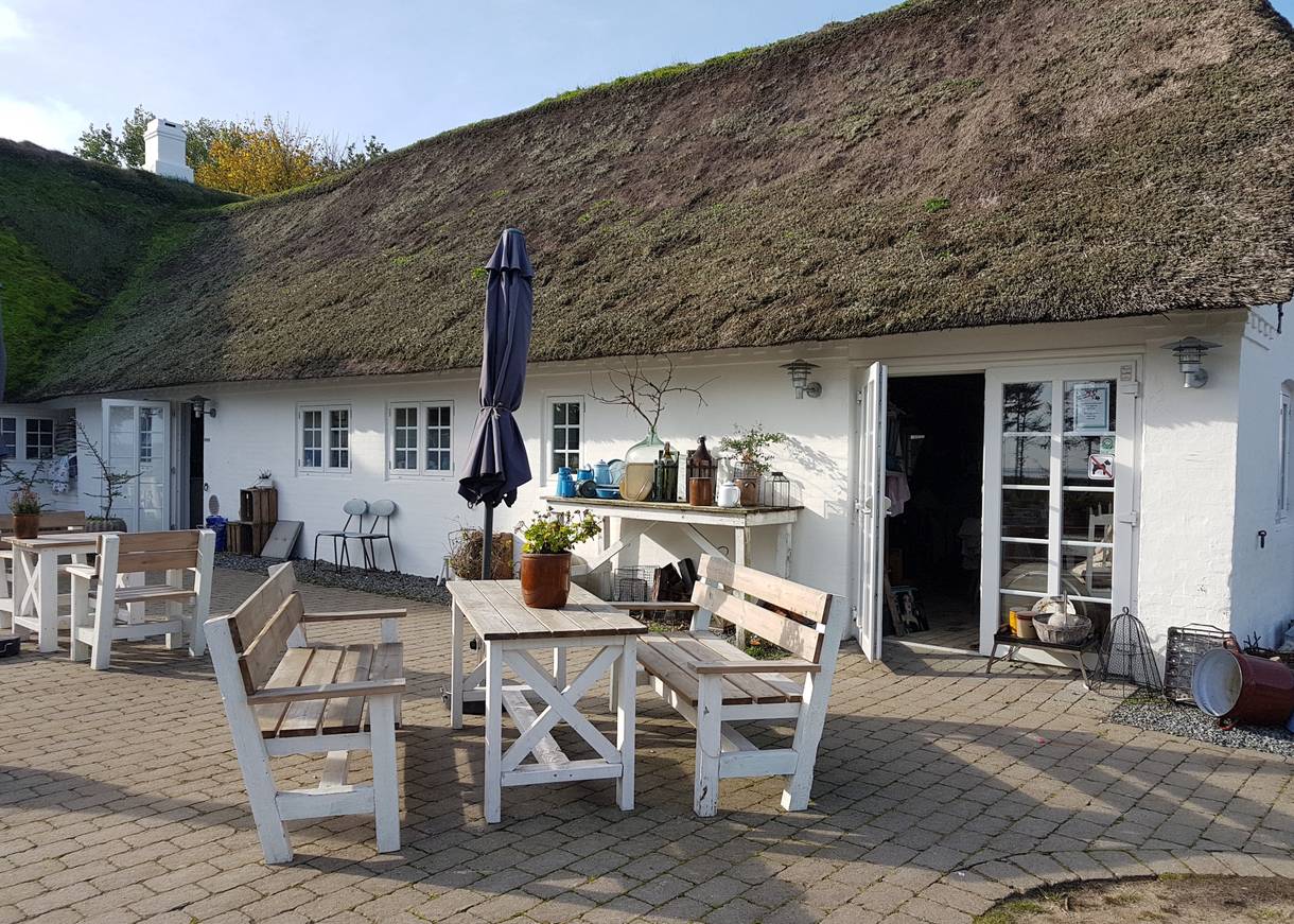 Gartenmöbel vor einem weißen Reetdachhof mit einem Café
