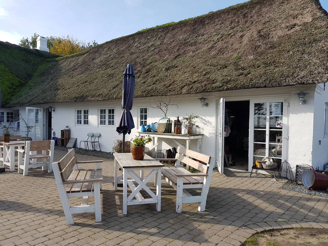 Gartenmöbel vor einem weißen Reetdachhof mit einem Café