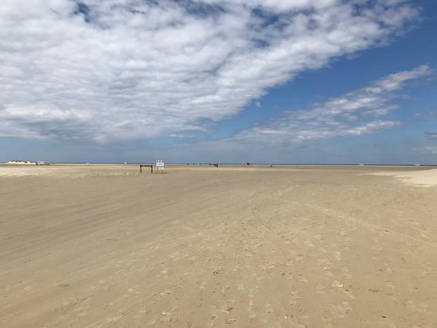 Strandzugang zu einem breiten Autostrand, im Hintergrund viele Autos und das Meer