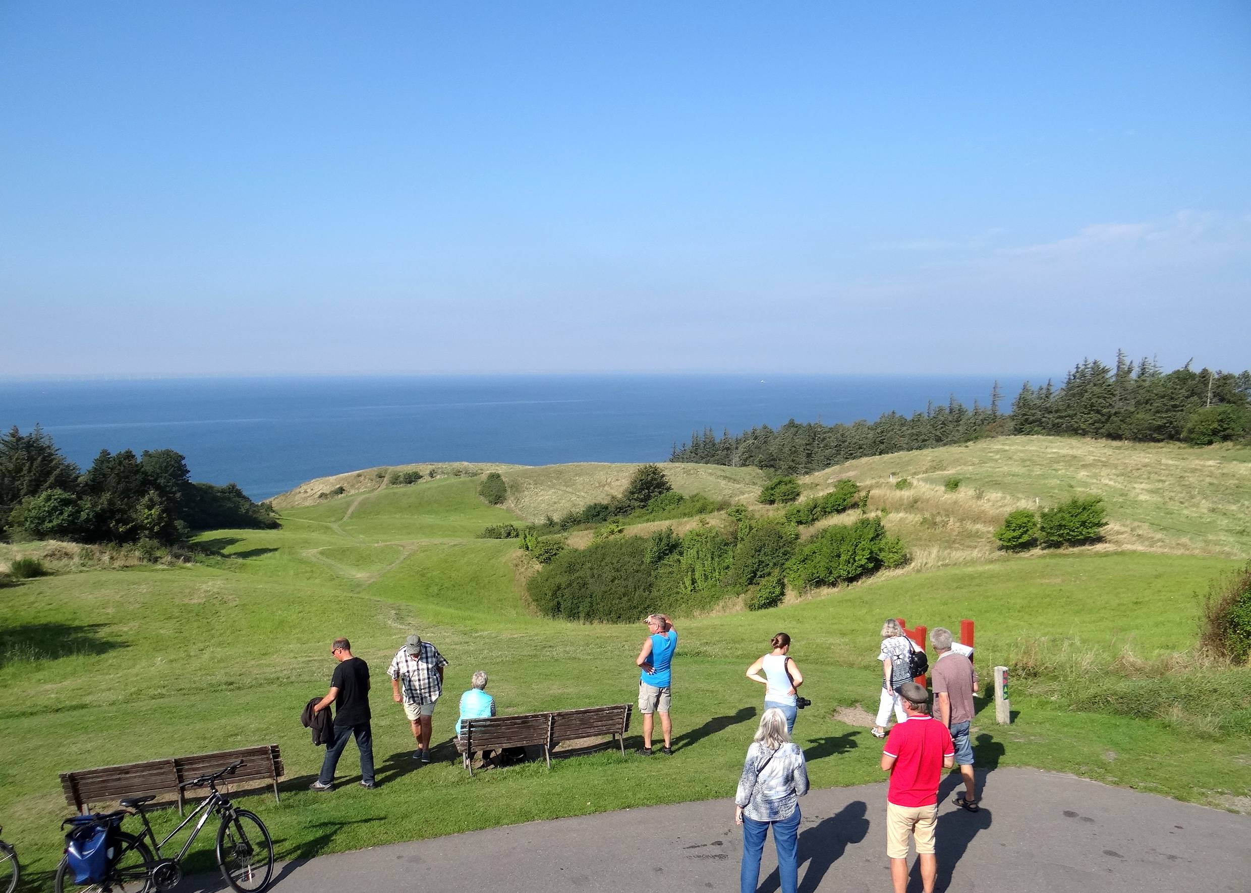 Urlauber vor Bänken auf einem Hügel mit Meerblick