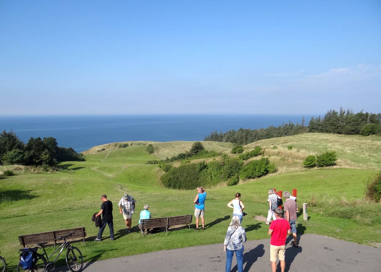 Urlauber vor Bänken auf einem Hügel mit Meerblick