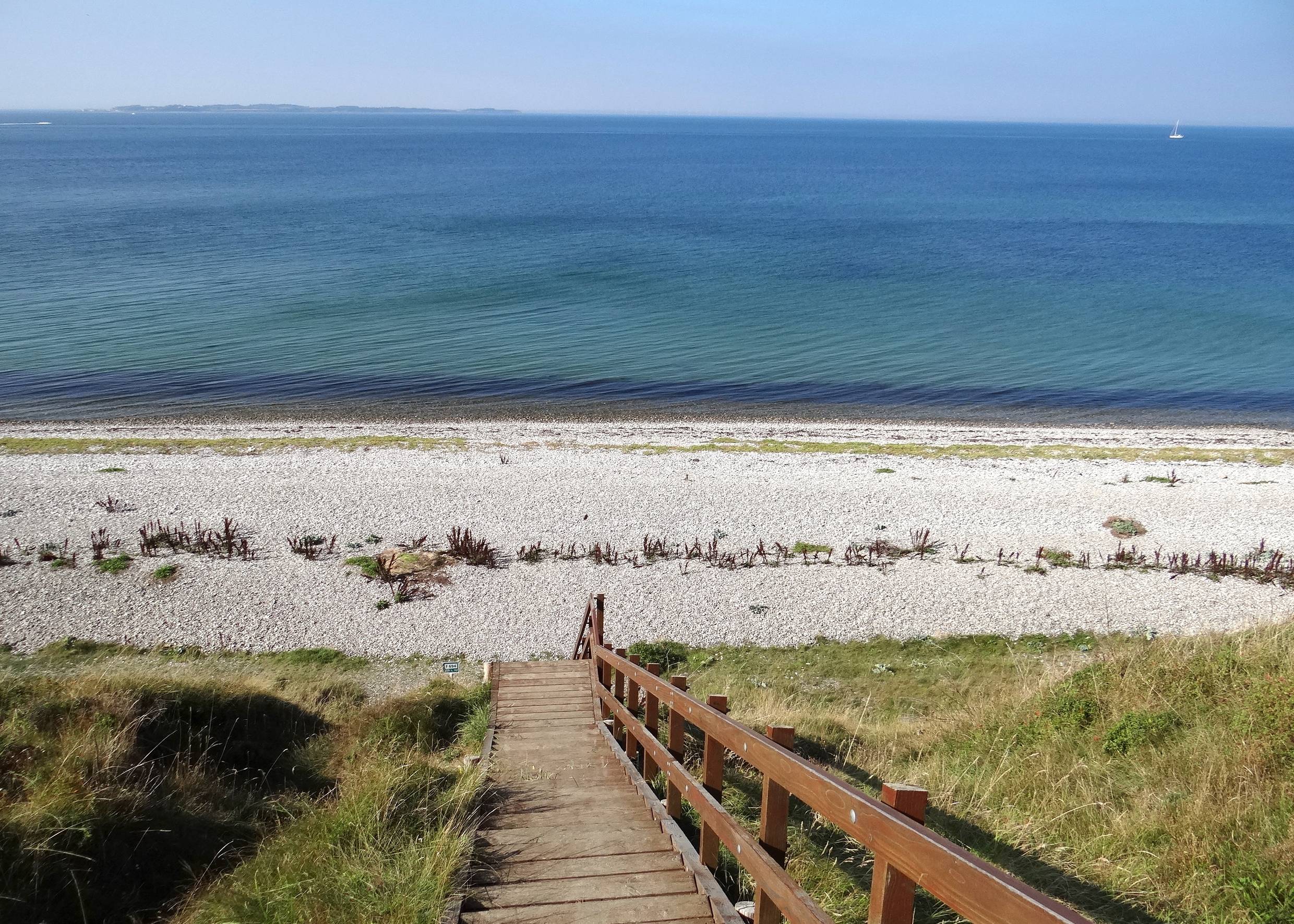 Steile Holztreppe, die zu einem Steinstrand führt