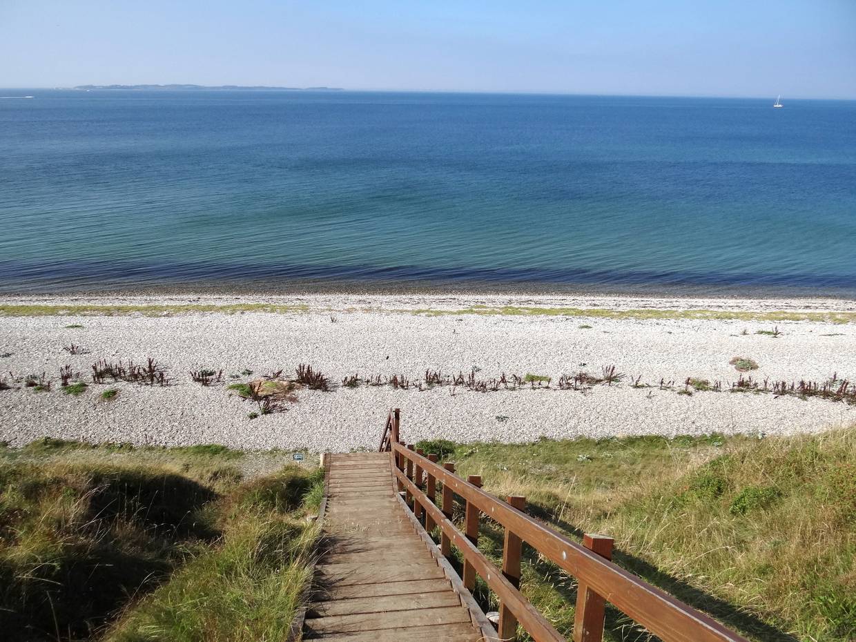 Steile Holztreppe, die zu einem Steinstrand führt
