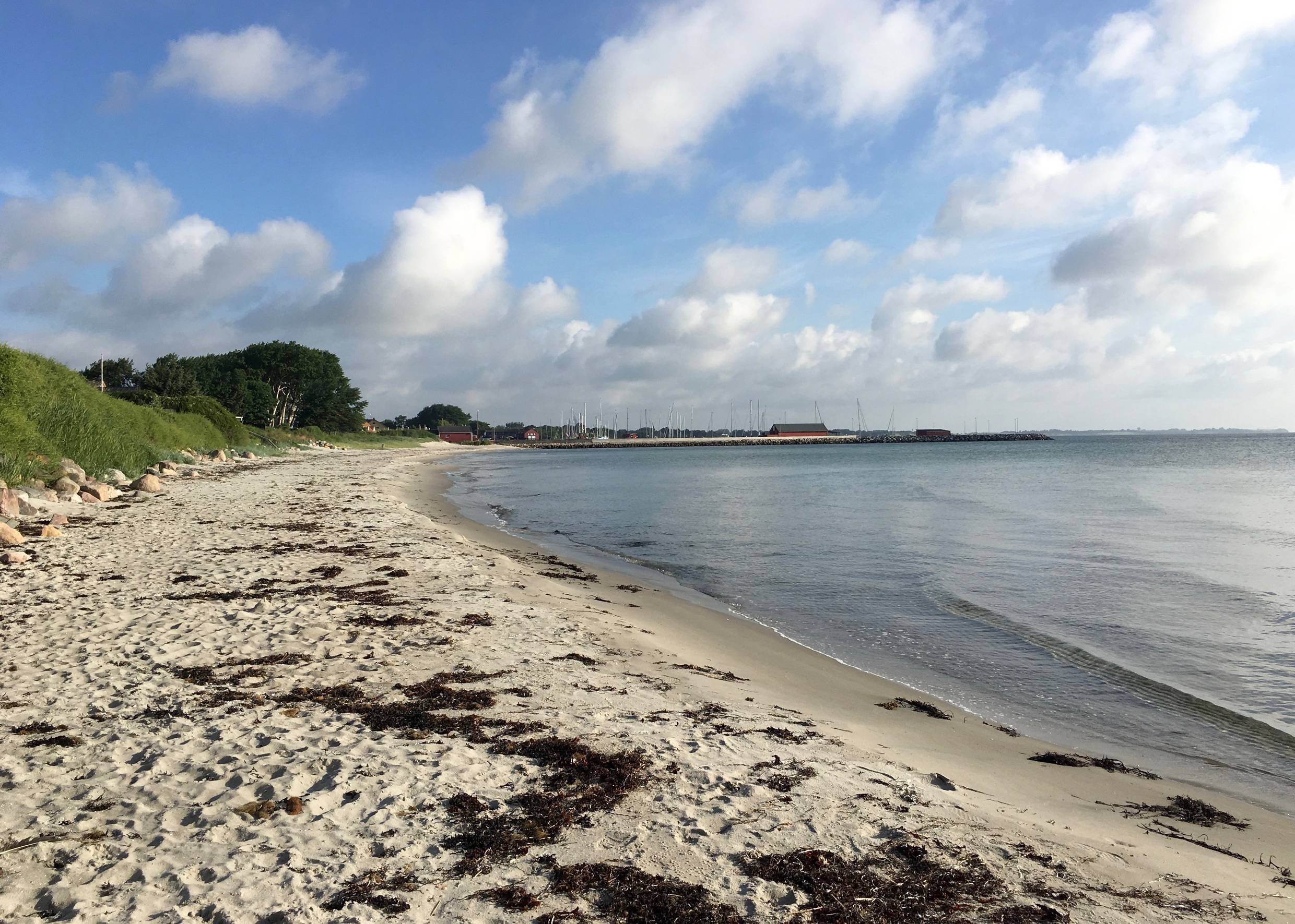 Sandbucht, in der Ferne ein Hafen mit Segeljachten