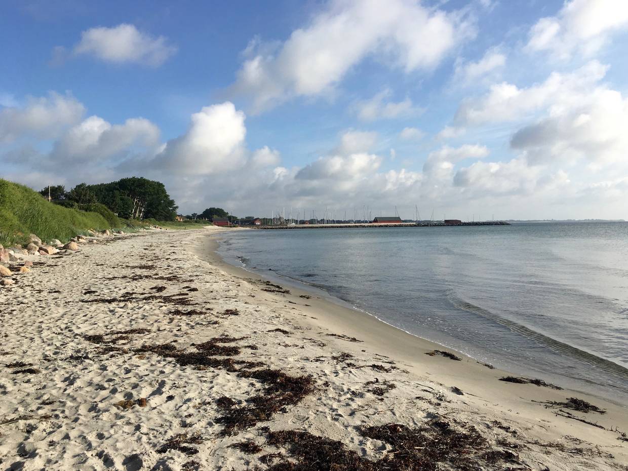 Sandbucht, in der Ferne ein Hafen mit Segeljachten