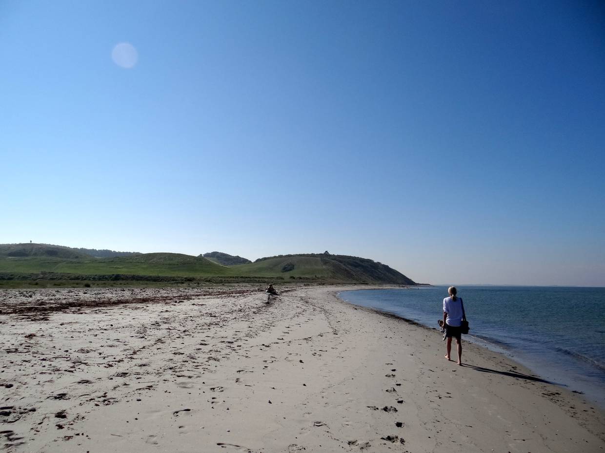 Spaziergängerin am Strand mit Hügeln im Hintergrund