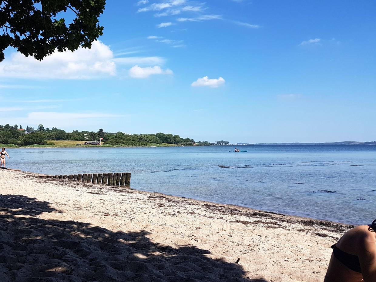 Sandstrand an einer Förde, auf dem Wasser ein Kajak