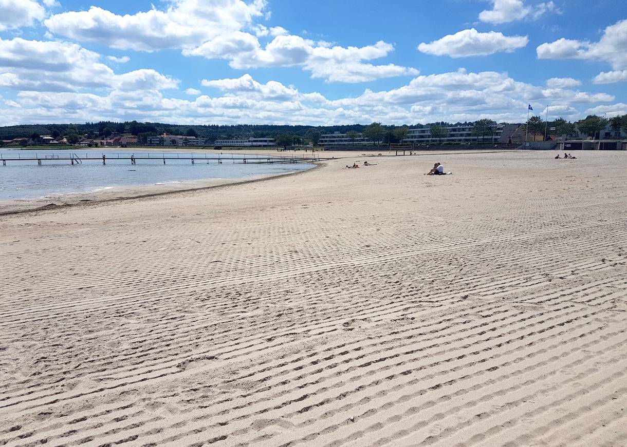 Breiter Sandstrand mit einem Badesteg und Wohnblocks im Hintergrund