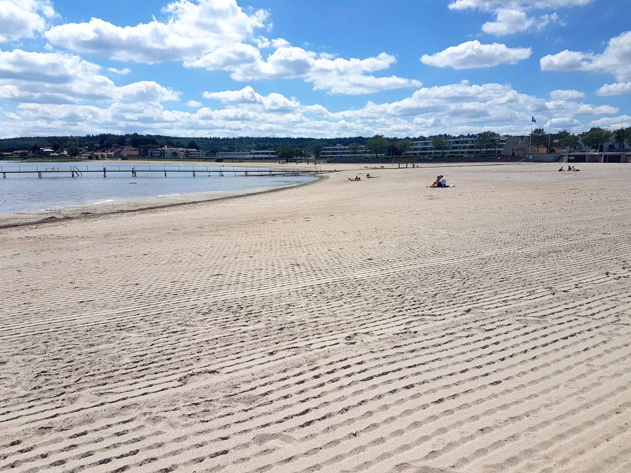 Breiter Sandstrand mit einem Badesteg und Wohnblocks im Hintergrund