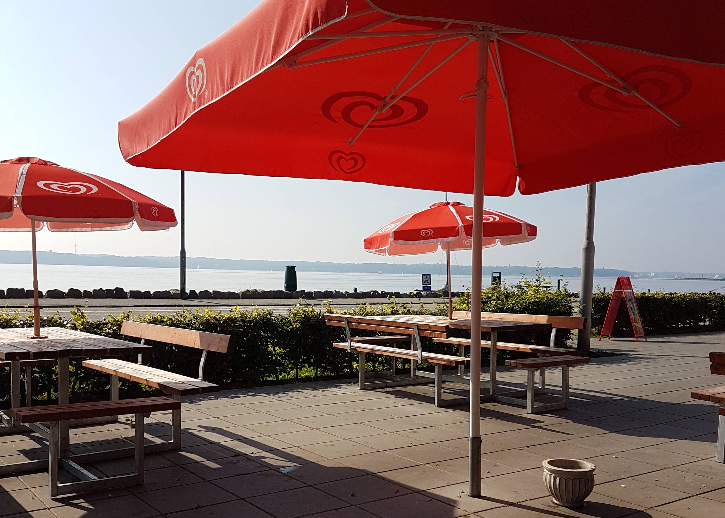Rote Sonnenschirme über Picknickbänken, dahitner die Flensburger Förd