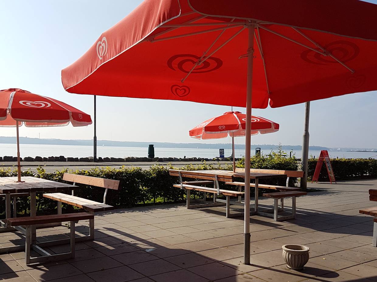 Rote Sonnenschirme über Picknickbänken, dahitner die Flensburger Förd