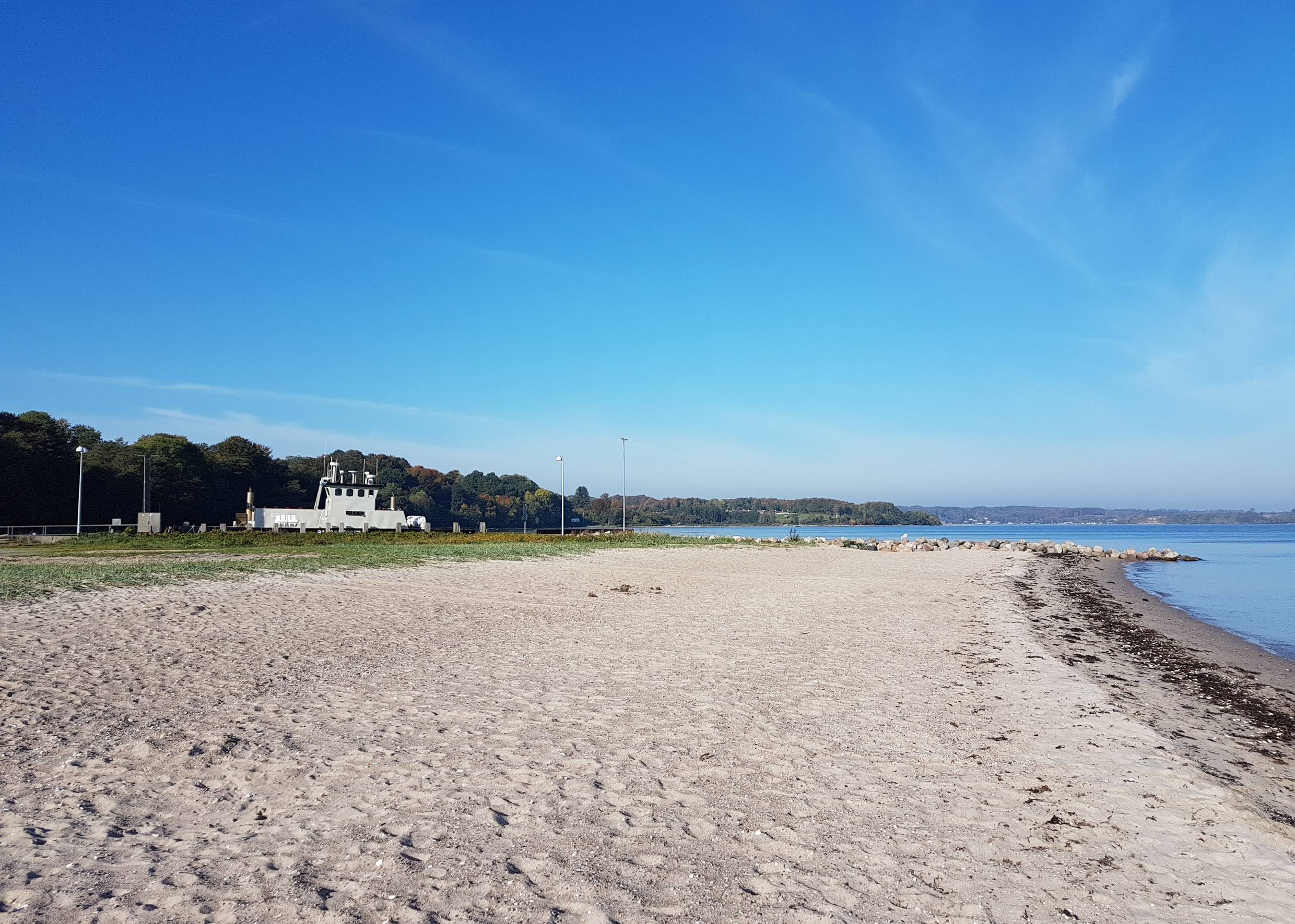Sandstrand, im Hintergrund eine kleine Fähre