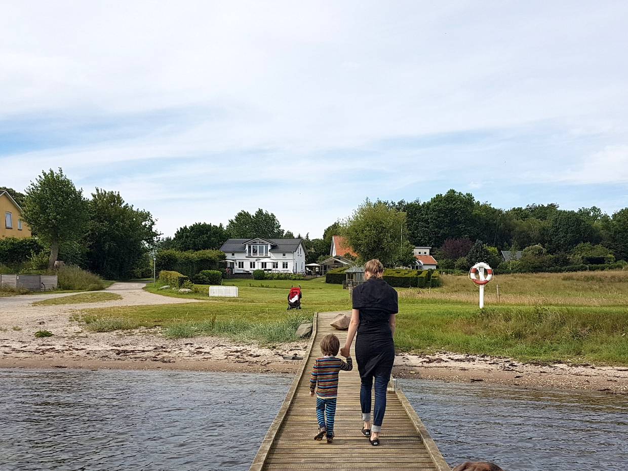 Mutter mit Kind auf einem Holzsteg, im Hintergrund Häuser im Grünen