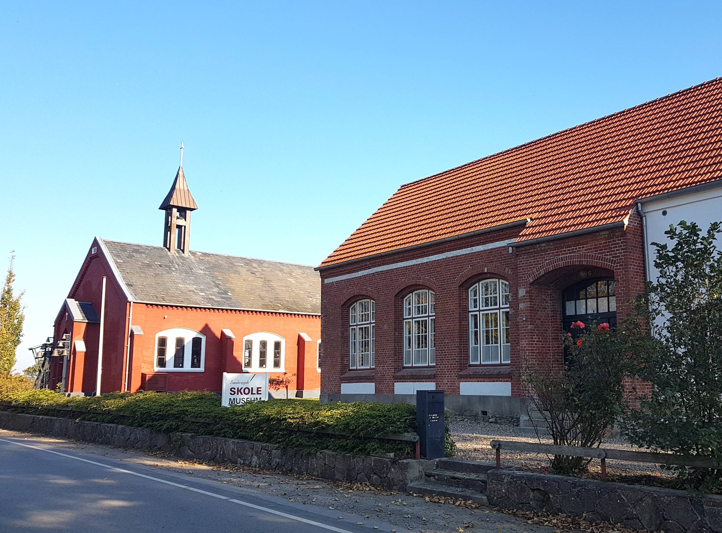 Rotes Haus, das an eine Kirche erinnert, daneben ein altes Schulhaus