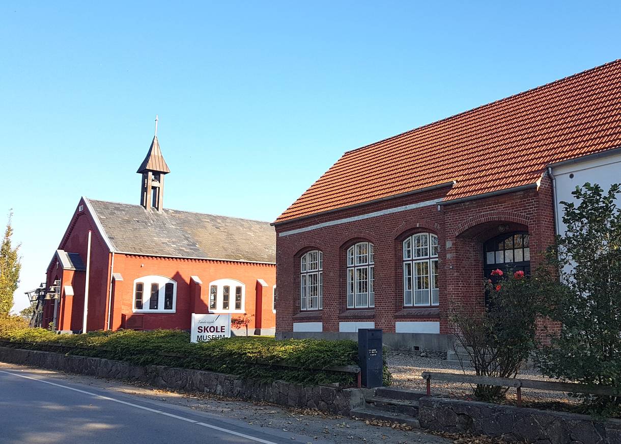 Rotes Haus, das an eine Kirche erinnert, daneben ein altes Schulhaus