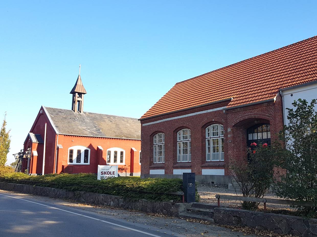 Rotes Haus, das an eine Kirche erinnert, daneben ein altes Schulhaus
