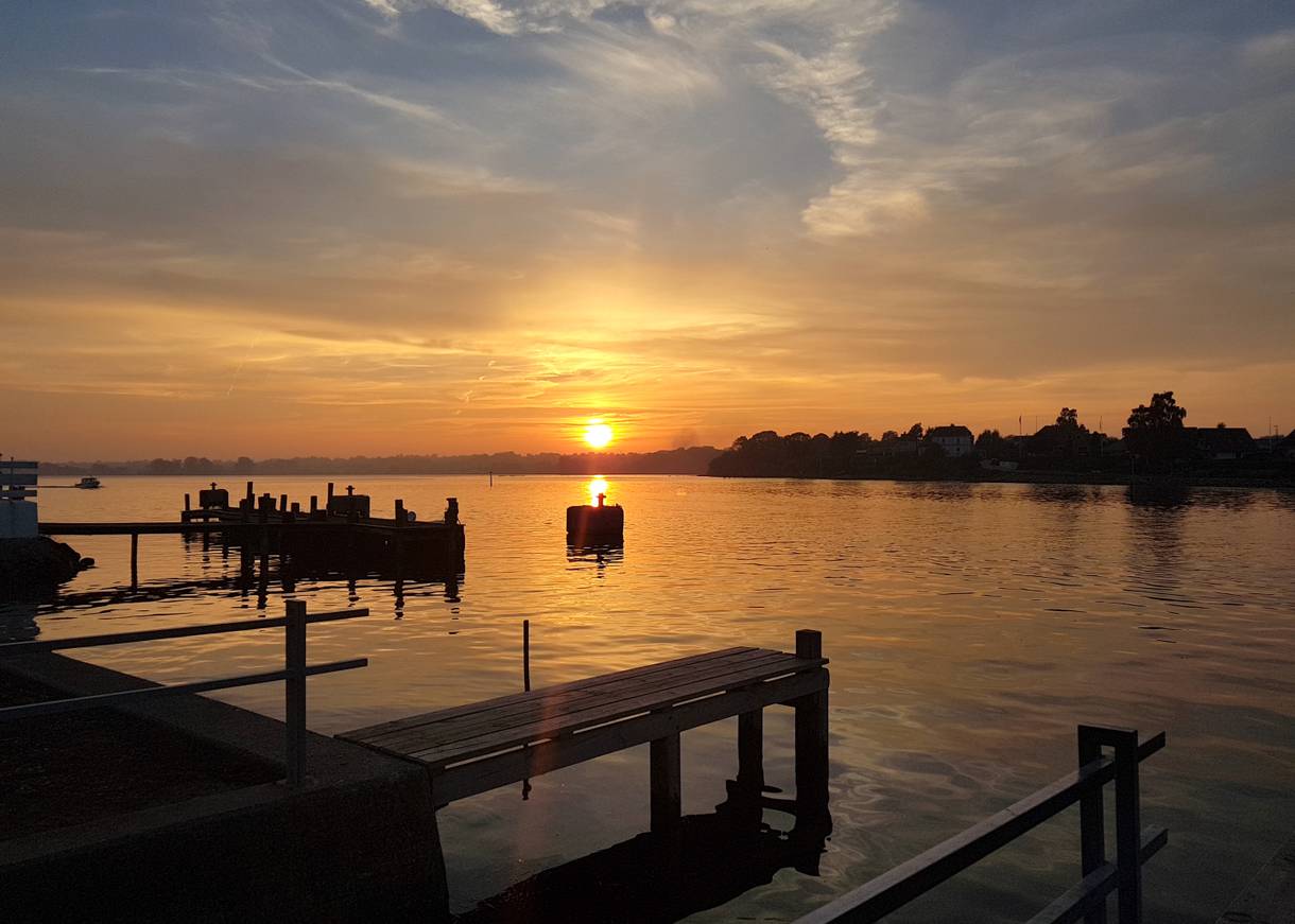 Sonnenuntergang über der flachen Ostsee mit Holzstegen und kleinen Booten im Bild