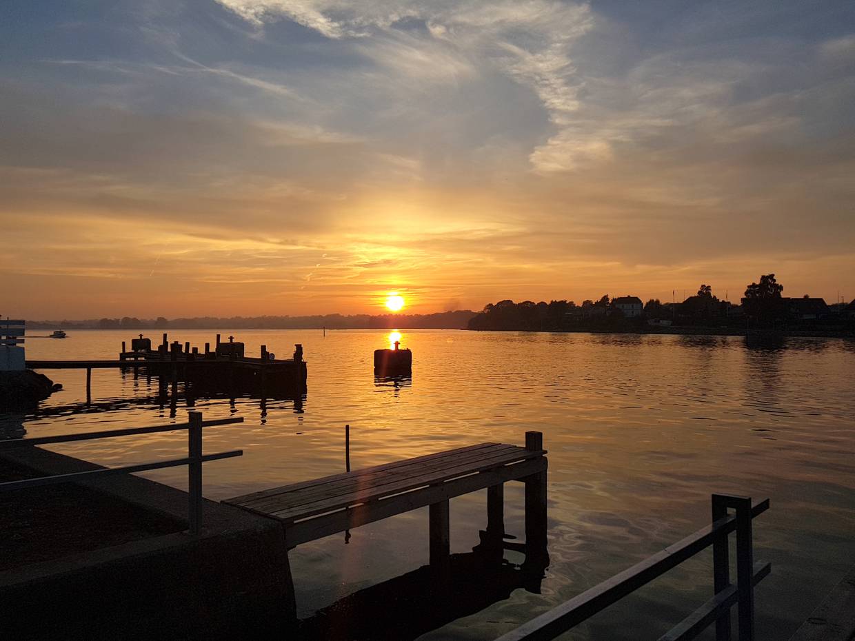 Sonnenuntergang über der flachen Ostsee mit Holzstegen und kleinen Booten im Bild