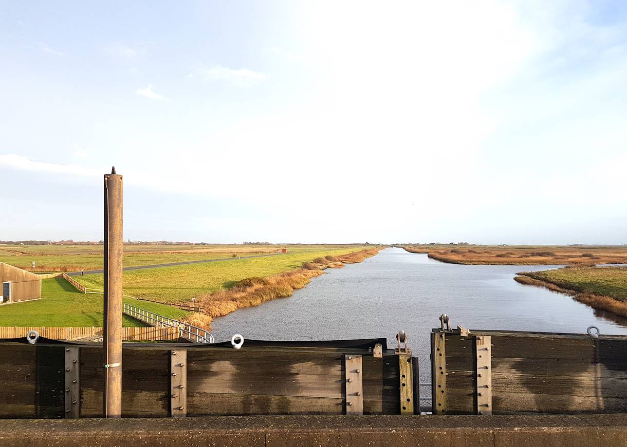 Blick von einer Schleuse auf einen schnurgerade Fluss in den Wiesen