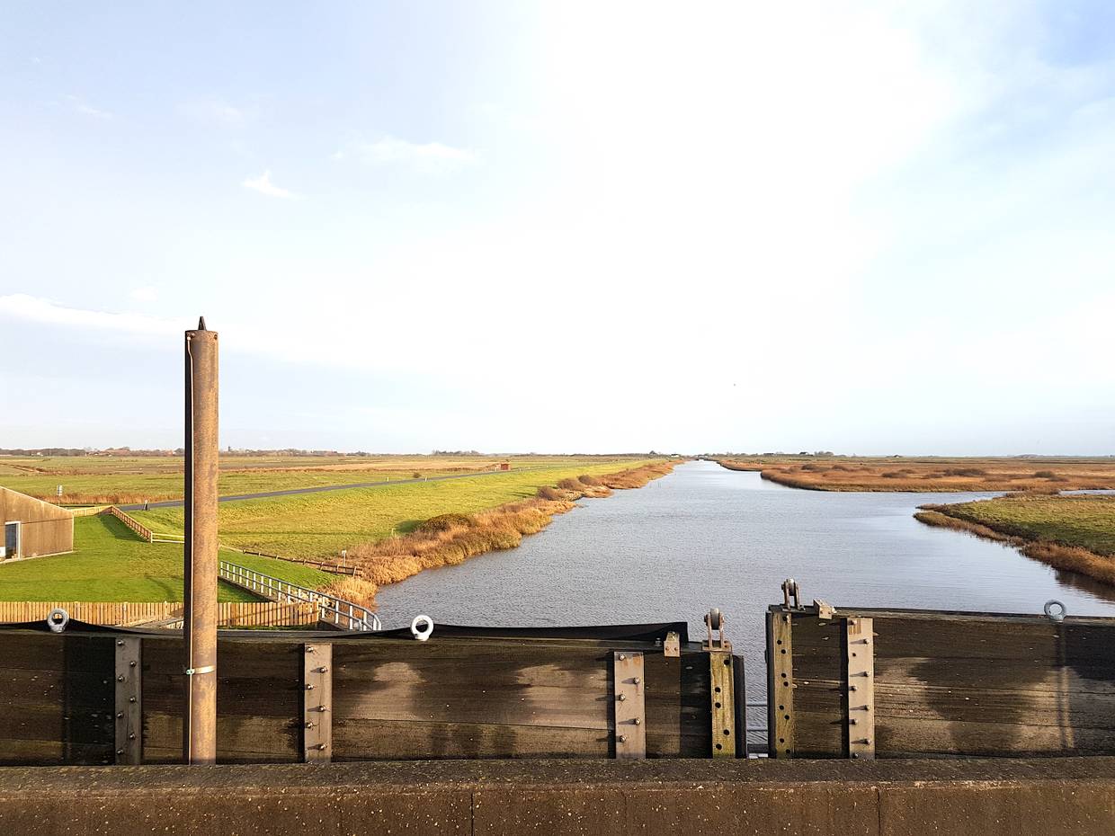 Blick von einer Schleuse auf einen schnurgerade Fluss in den Wiesen